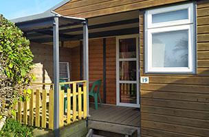 Vue du chalet 1 chambre 2 personnes avec terrasse intégrée couverte avec salon de jardin, en location au camping à l’Abri de l’Océan dans le Morbilhan